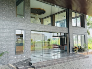 A modern building with a stone facade, large glass windows, and a balcony with outdoor seating.