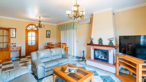 Una sala de estar con sofá, mesa de centro, chimenea, televisor y una araña.