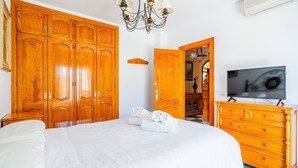 Un dormitorio con una cama grande, un armario de madera, televisor y una araña.