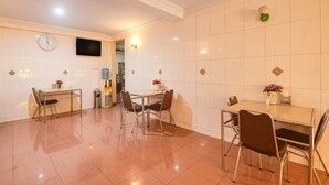 A dining area with a table and chairs, a clock on the wall, and a television mounted above. - Luxury Deluxe DBL Retreat W/ Free Wifi and Parking (Makassar)
