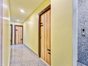 A hallway with wooden doors, a carpeted floor, and a wall-mounted intercom. - Hotel O Downtown INN (Barasat)