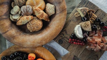 A wooden bowl filled with various breads and pastries, a wooden board with cheeses, nuts, and grapes, and a bowl of cherries and apricots.