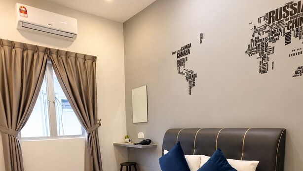 A hotel room with a bed, a ceiling fan, an air conditioning unit, a desk with a chair, and a window with curtains.