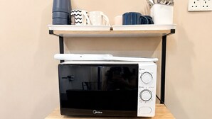 A microwave oven on a shelf, a stack of plates, and a kettle on a table.