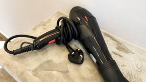 A black hairdryer with a red cord and a black attachment on a beige surface.