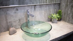 A bathroom with a glass bowl sink, a faucet, a soap dispenser, and a potted plant.