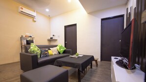 A living room with a sofa, a coffee table, a TV, and a small kitchenette.