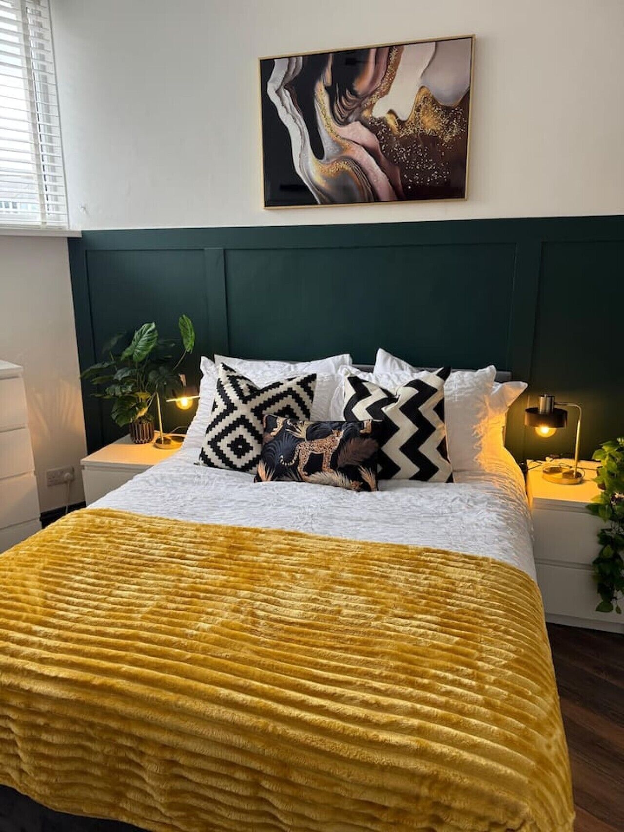 A bed with a yellow blanket, a dark green headboard, and patterned pillows.