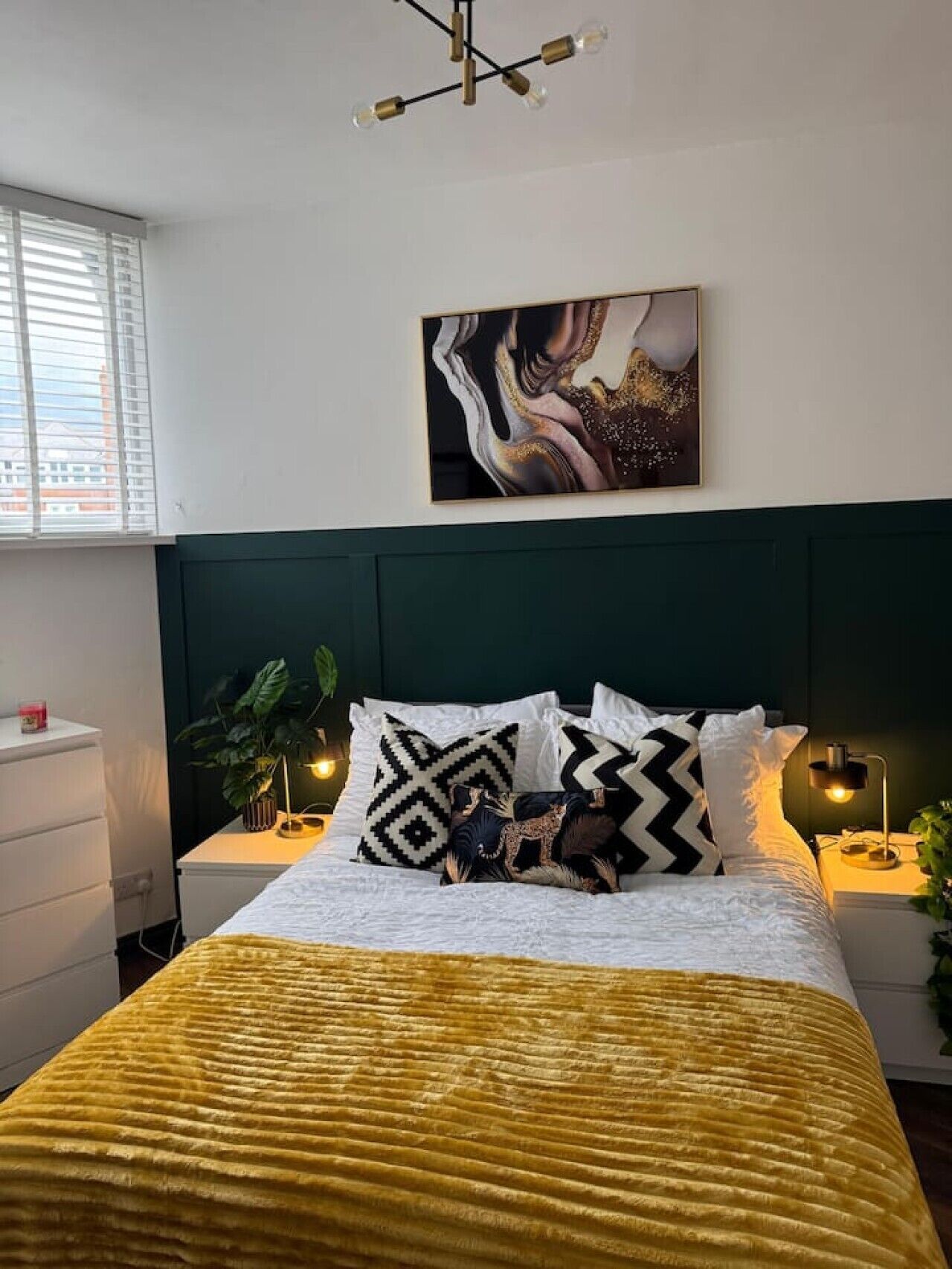 A bedroom with a bed, a painting, bedside lamps, a nightstand, and a window.