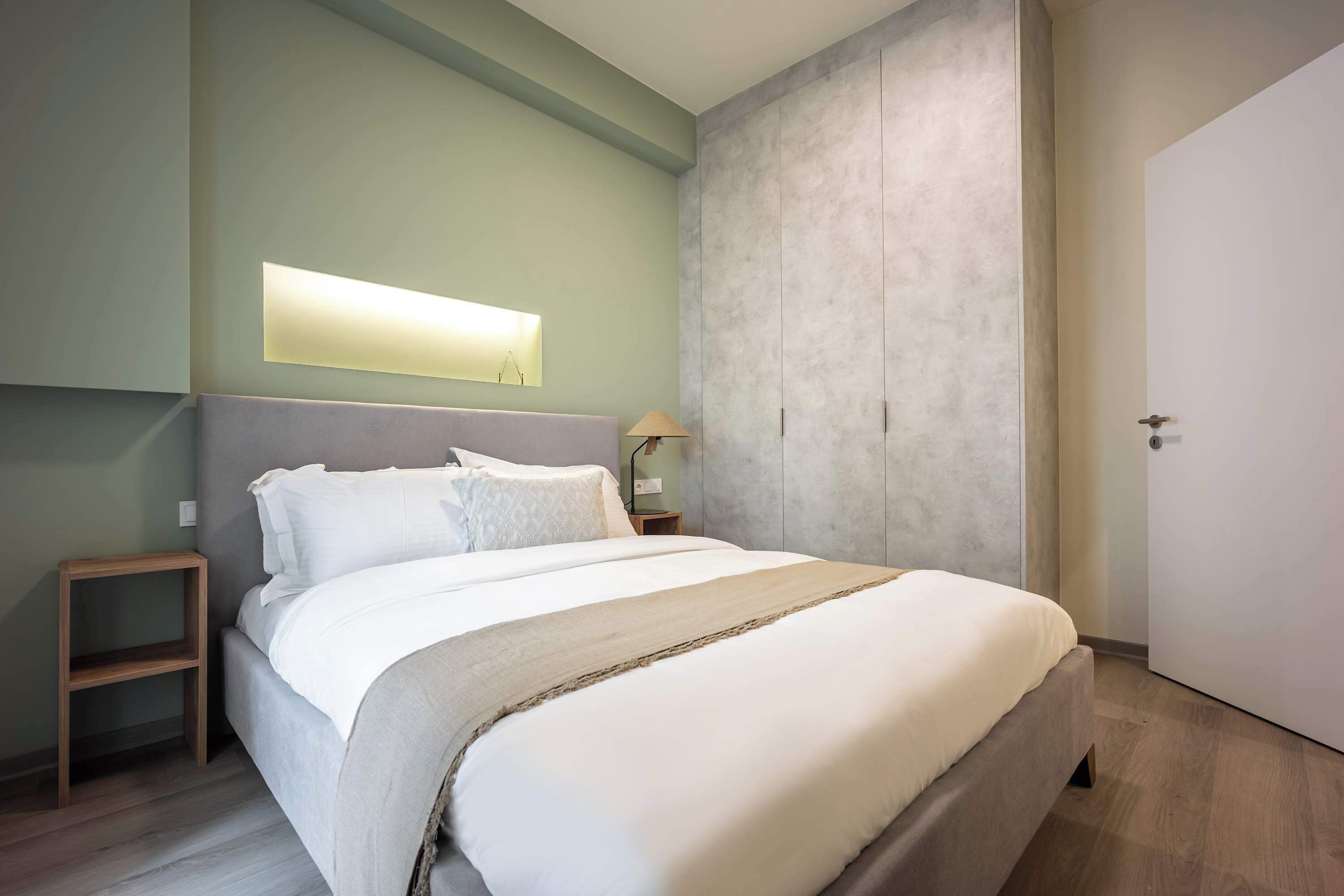 Un dormitorio moderno con una cama grande, mesitas de noche, un armario y un aplique de pared.