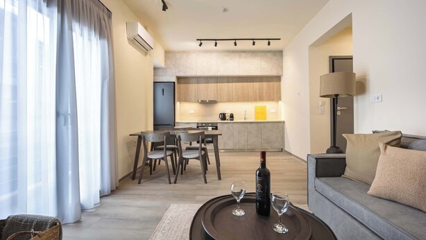 A modern living room with a sofa, a dining area with chairs, a kitchen in the background, and a large window with curtains. - Stylish 2BR Exarchia l King Bed & Desk (Exarchia)