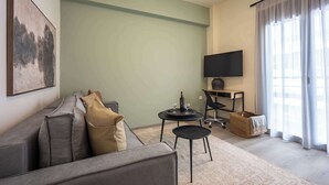 A living room with a sofa, a small table with a bottle and glasses, a TV on a stand, and a large window with curtains. - Stylish 2BR Exarchia l King Bed & Desk (Exarchia)