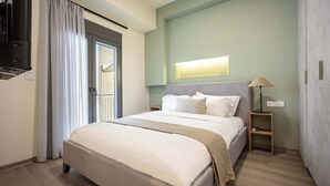 A hotel room with a bed, a TV, a bedside table with a lamp, and a window with curtains. - Stylish 2BR Exarchia l King Bed & Desk (Exarchia)