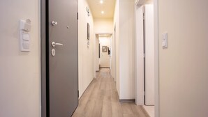 A hallway with a wooden floor, a door with a key lock, a light switch, and a wall-mounted light fixture. - Stylish 2BR Exarchia l King Bed & Desk (Exarchia)