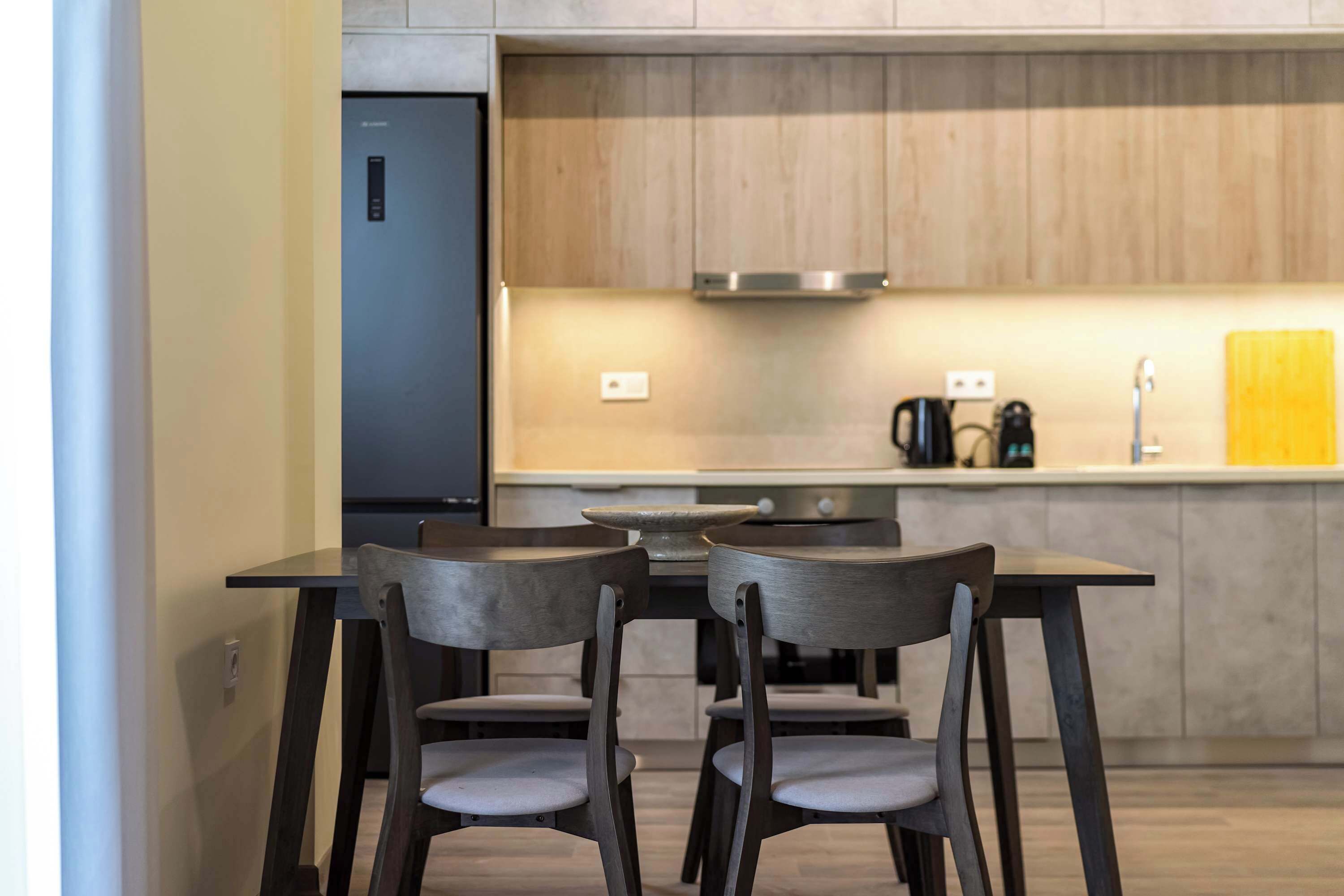 Une cuisine moderne équipée d’un four encastré, d’une machine à café et d’une planche à découper jaune posée sur le plan de travail.