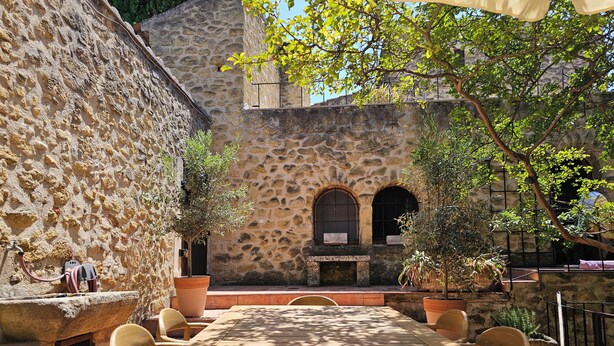 An outdoor dining area with a stone wall, wooden table, and chairs. - Beautiful Village House (Lauris)