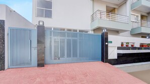 A gated entrance with a metal gate and a red-tiled pathway leading to a building with a balcony. - Deluxe Pine Villa (Lucknow)