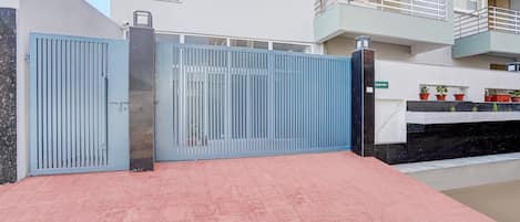 A gated entrance with a metal gate and a red-tiled pathway leading to a building with a balcony.