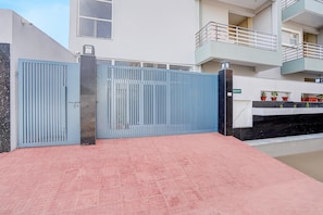 Una entrada tancada amb una reixa de metall i un camí empavedat de teules vermelles que condueix a un edifici amb un balcó.