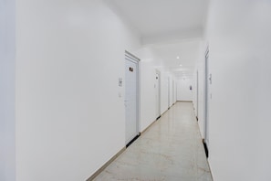 Un pasillo largo y estrecho con paredes y puertas blancas, que conduce a varias habitaciones.