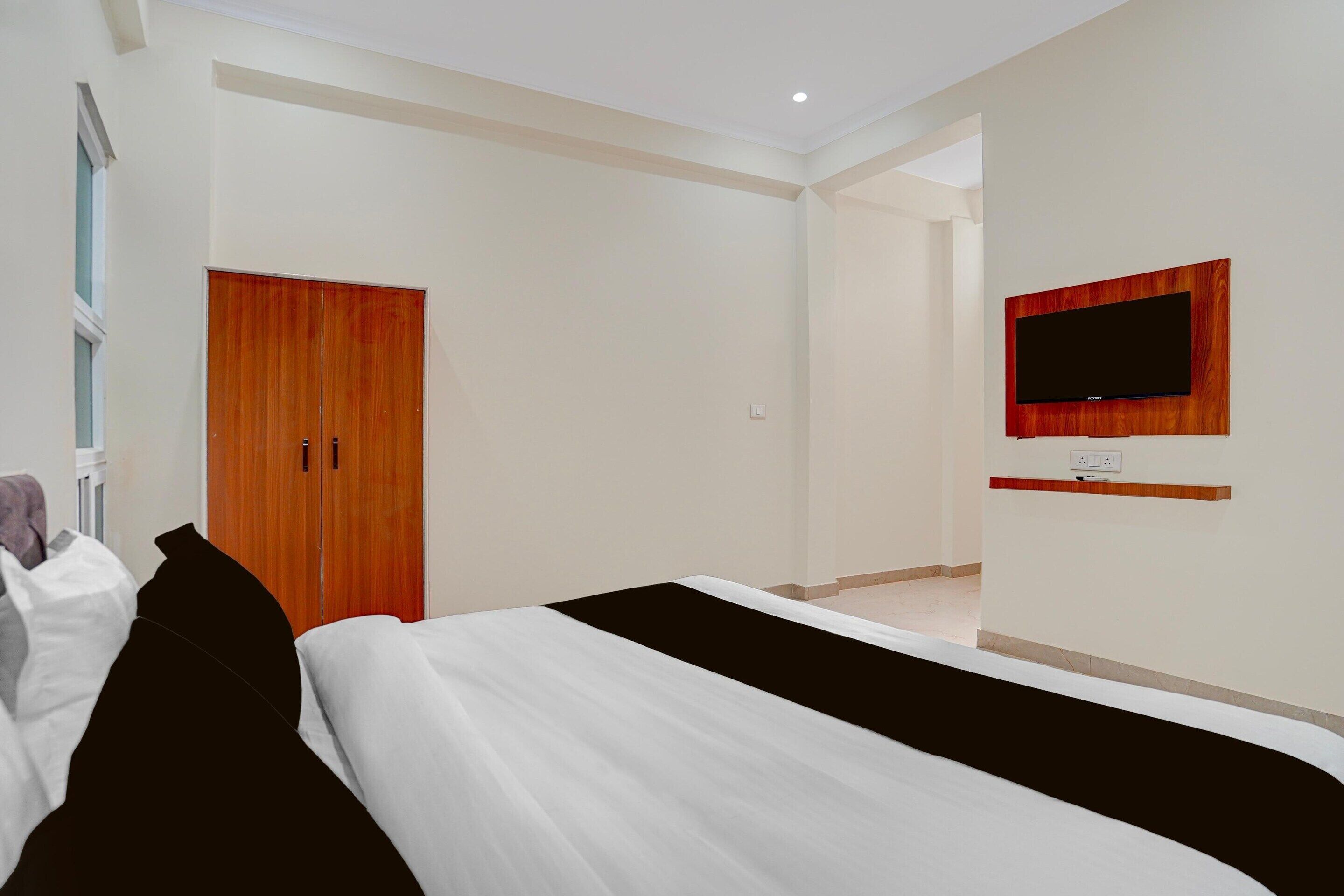 A hotel room with a bed, a wardrobe, a television mounted on the wall, and a door leading to another room.