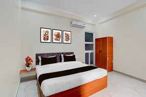 A bedroom with a bed, a nightstand, a wardrobe, and three framed artworks on the wall. - Deluxe Pine Villa (Lucknow)
