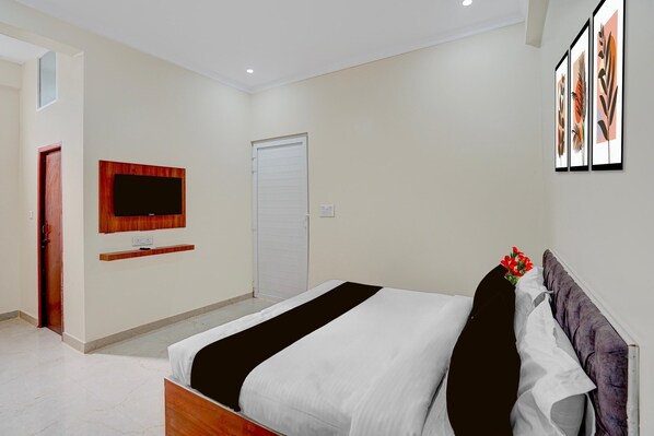 A bedroom with a bed, a television mounted on the wall, a door, and a framed picture above the bed.