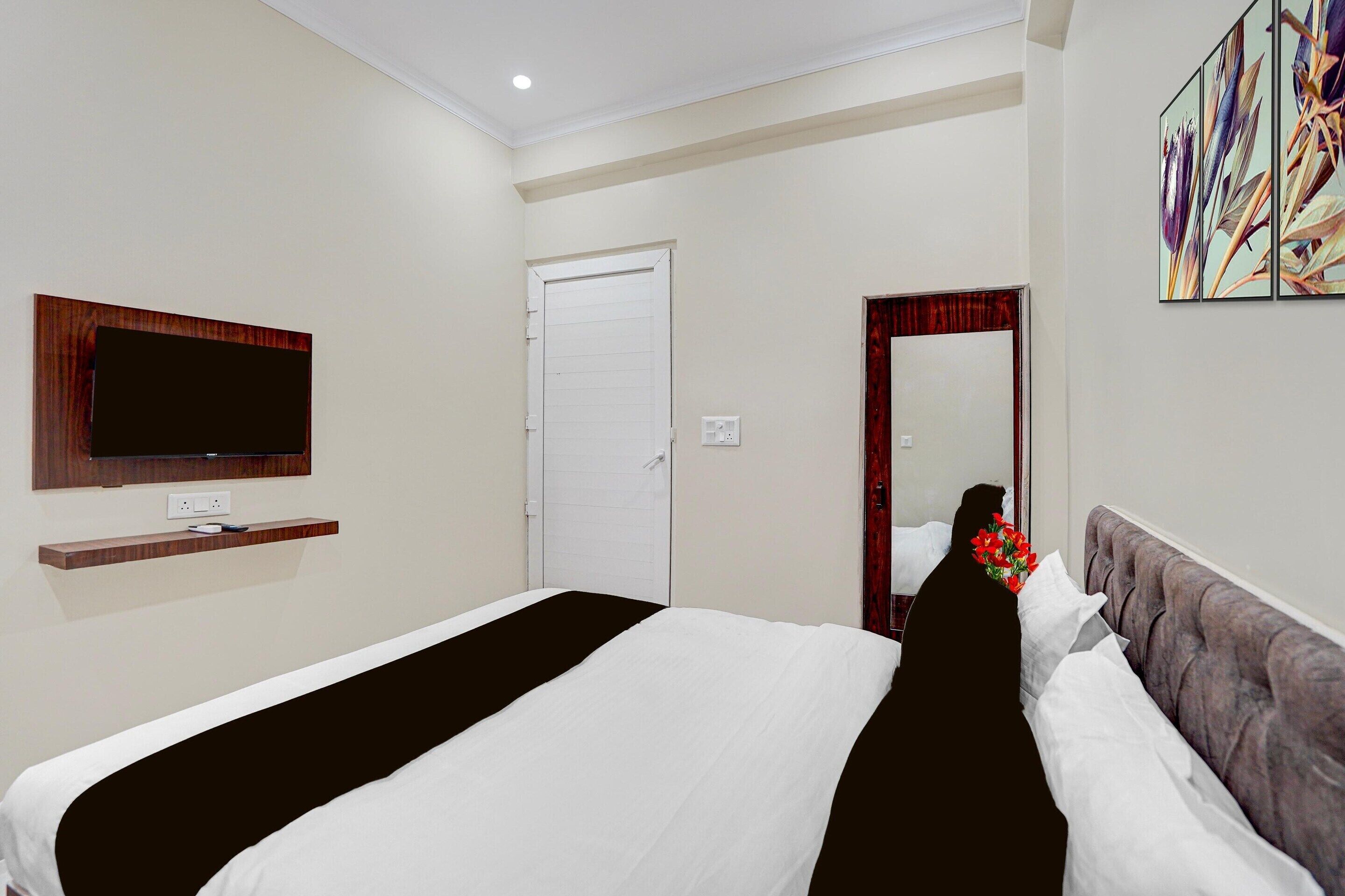 A hotel room with a bed, a television mounted on the wall, a door, and a mirror.