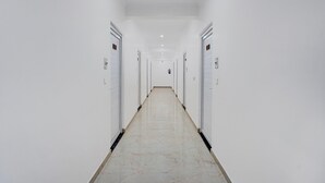 A long, narrow hallway with white walls and doors, leading to a distant end. - Deluxe Pine Villa (Lucknow)