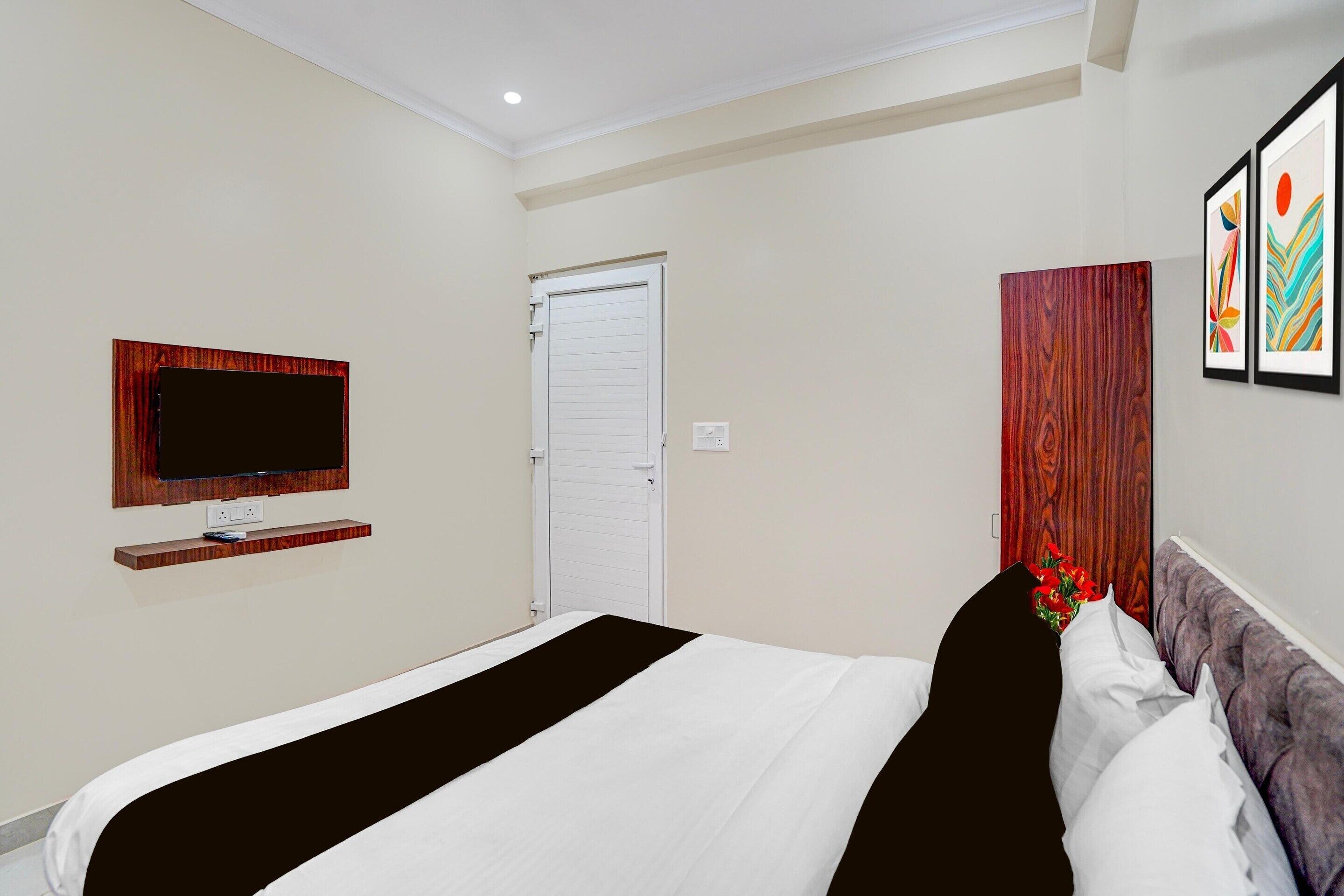 Ein Hotelzimmer mit einem Bett, einem Wandtelevisor, einer Tür und einem an der Wand hängenden Kunstwerk.