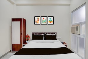 Ein Hotelzimmer mit einem Bett, einem Kleiderschrank, einem Nachttisch, einer Vase mit Blumen und drei gerahmten Bildern an der Wand.