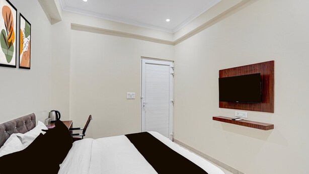 A hotel room with a bed, a TV mounted on the wall, and a door. - Deluxe Pine Villa (Lucknow)
