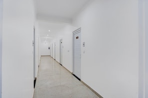 Un long couloir étroit aux murs et aux portes blancs, qui mène à une pièce où l’on peut voir un panneau indiquant un numéro.