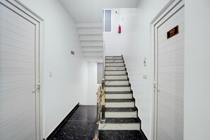 A hotel hallway with a marble staircase, white doors, and a fire extinguisher mounted on the wall.