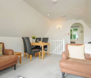Ein Loft-Zimmer mit Esstisch, zwei schwarzen Stühlen, einem braunen Sofa und einem weißen Geländer.