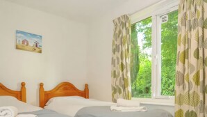 Quarto com duas camas, janela com cortinas, um quadro na parede e uma pequena mesa de cabeceira.
