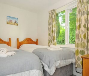 Ein Schlafzimmer mit zwei Betten, einem Fenster mit Vorhängen, einem Bild an der Wand und einem kleinen Nachttisch.