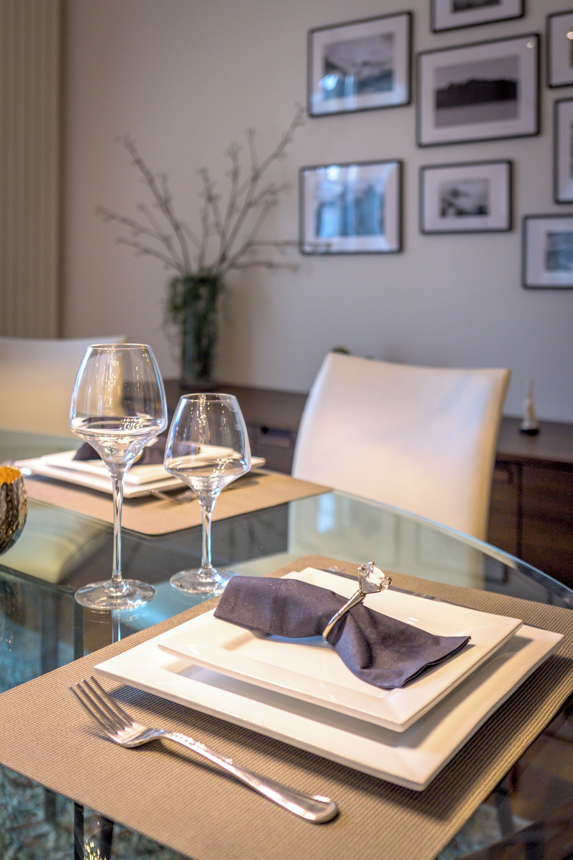 Une table à manger avec deux verres à vin, une fourchette et une serviette sur une table en verre.