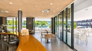 En moderne restaurant med en buet trædisk, store vinduer og udsigt til udesiddepladser.