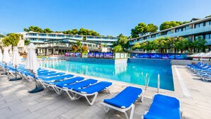 En swimmingpool med blå liggestole og parasoller, omgivet af en hotelbygning med moderne arkitektur.