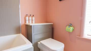 Un baño con inodoro, lavabo y estante con tres botellas.