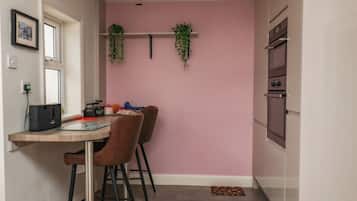 A kitchen with a pink wall, two hanging plants, a dining table with chairs, and a refrigerator.