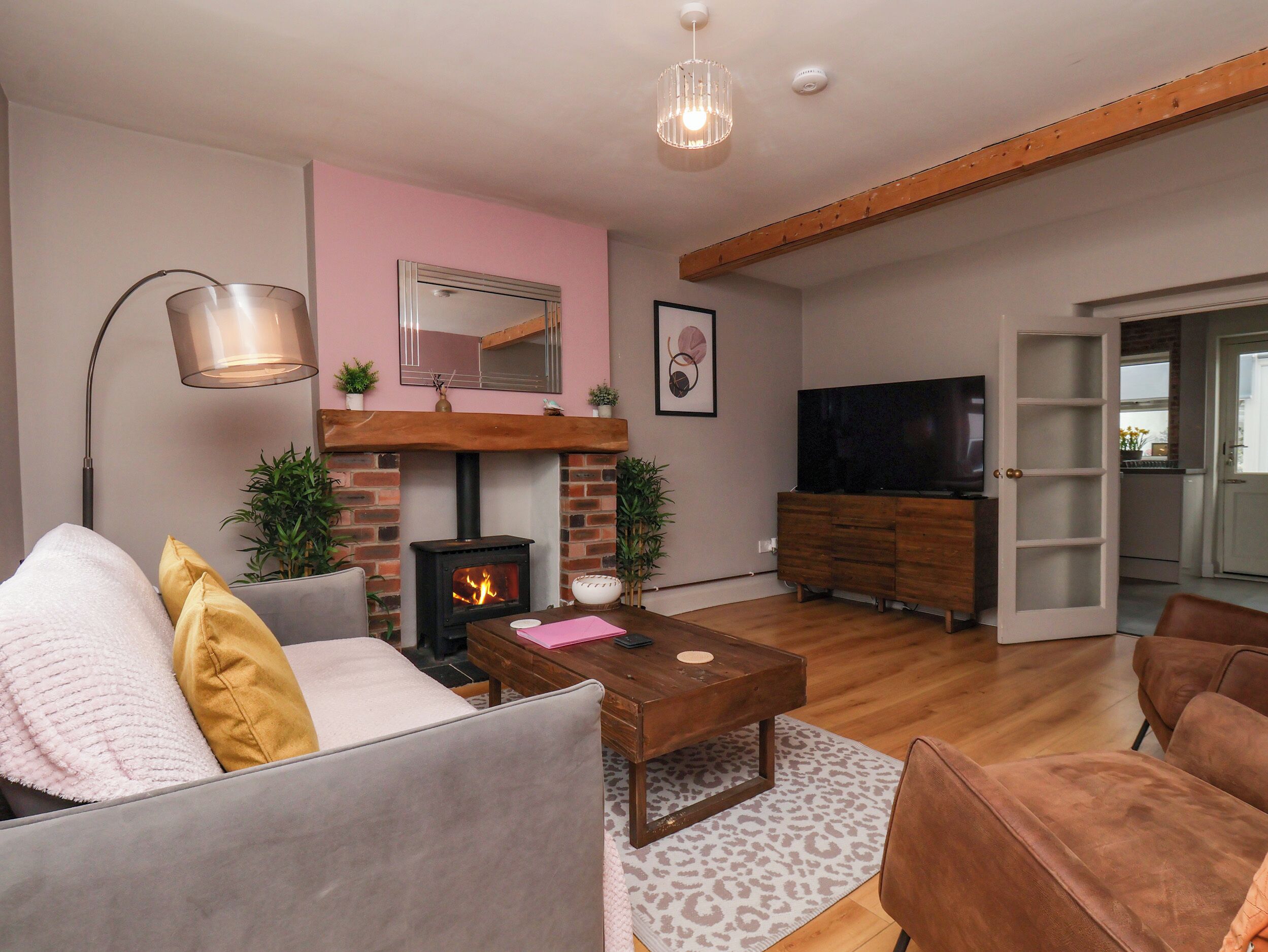 Sala de estar con chimenea, sofá, mesa de centro, televisor y una cocina visible a través de un umbral abierto.