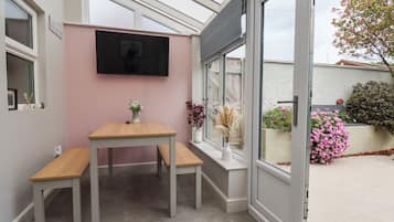 A conservatory with a table, chairs, a TV, and a view of the outside.