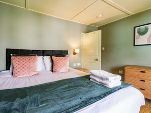 A neatly made bed with patterned pillows, a green throw blanket, and a wooden nightstand with a lamp.