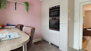 Une cuisine moderne avec des armoires blanches, un four encastré et un coin repas comprenant une table ronde et une chaise en cuir.