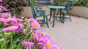 Une terrasse avec une table ronde et deux chaises, entourée de fleurs roses.