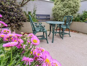 A patio with a round table and two chairs, surrounded by pink flowers. - The Braes (Redcar)
