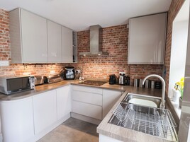 Una cocina compacta con armarios blancos, pared de ladrillo, pileta de acero inoxidable y escurreplatos.