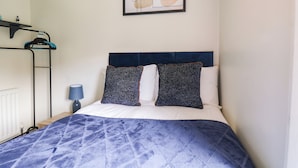 A bedroom with a bed, a headboard, a wall-mounted picture, a radiator, and a shelf with items. - The Braes (Redcar)